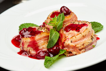 Gourmet bacon-wrapped chicken rolls with cherry sauce, garnished with mint, perfect for fine dining