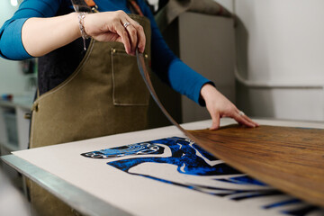 Hand of young female worker of modern typography center creating new artwork while standing by printing machine in workshop