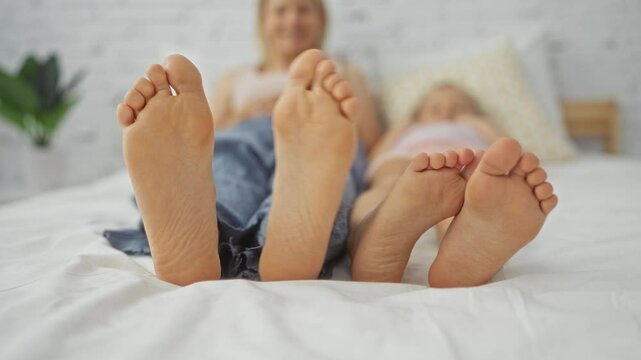 Woman and child lying together on a bed indoors showing their feet in a cozy home bedroom setting