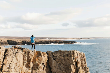 Fototapeta premium Hiker overlooking rugged coastline at sunset