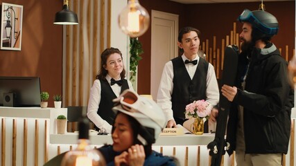 Customer wonders where the ski slope is and asks receptionist for directions at wintertime alpine resort. Man equipped with outerwear and protective helmet carrying skis for winter sport.