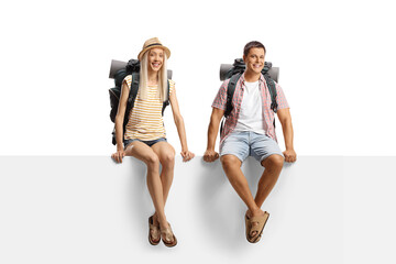 Obraz premium Male and female backpackers sitting on a blank panel and smiling