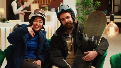 POV of couple chatting on videocall and wearing winter sport clothes with protective helmets, people preparing to go skiing on alpine slopes. Guests answering call on video connection. Tripod shot.