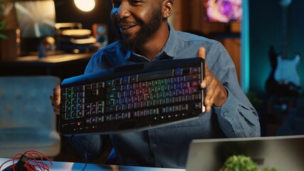 Content creator in dimly lit living room using camera to film RGB lights keyboard review for online streaming platforms. Media star hosts tech internet show, unboxing peripherals