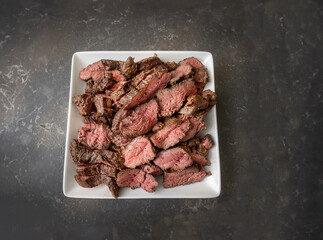 Carved bar-b-qued medium rare steak showing texture on a white plate on a grey granite countertop