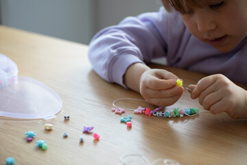 A sweet girl enthusiastically makes a bracelet of beads. A creative child engaged in jewelry making