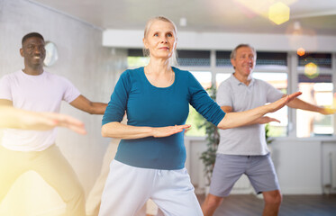 Obraz premium Positive emotional senior woman learning to dance krump with group in modern choreographic studio