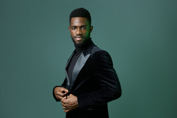 Elegant african american man in black tuxedo posing confidently against vibrant green background