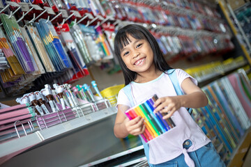 A young girl is smiling and holding a box of colored pencils