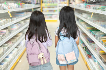 Two young girls are walking down a store aisle, looking at school supplies