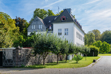 Beautiful white house surrounded by trees and greenery, situated inside the grounds of Klosterruine Heisterbach, with a peaceful sky above.
