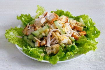 Crunchy salad with chicken, cheese, bread chips and cucumber with lettuce and garlic on a white plate. Healthy eating