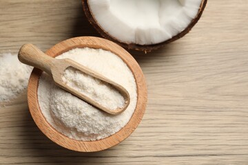 Fresh coconut flour in bowl, scoop and nut on wooden table, top view. Space for text