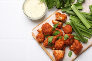 Baked cauliflower buffalo wings with parsley served on white tiled table, flat lay