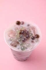 Tasty milk bubble tea in plastic cup on pink background, closeup