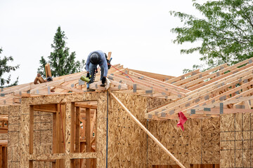 New residential home construction in framing stage, workman on the roof rafters working with...