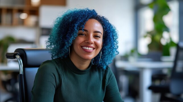 A cheerful woman with blue curly hair, seated in a modern office environment, radiating positivity and confidence.