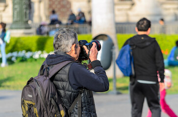 Hombre mayor con cámara fotográfica profesional enfocando al frente en una plaza