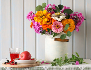 bright garden flowers, an apple and a currant on a white table convey the summer mood in a cozy wooden cottage.