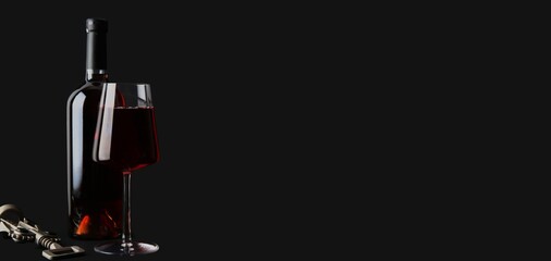 Bottle and glass of red wine on black background with space for text