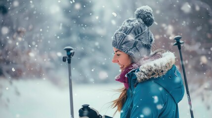 A woman in a blue jacket and a grey beanie smiles as snow falls around her. She is holding ski poles and is enjoying the winter weather.