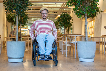 Relaxed confident disabled man in wheelchair leaving cafe, sitting between two potted trees, facing camera. Accessible public space encourages active lifestyle, provides comfort in outdoor areas