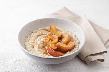 Sweet oatmeal porridge with baked apple slices, cinnamon and caramel sauce in a gray bowl on a light background, top view. Delicious homemade food
