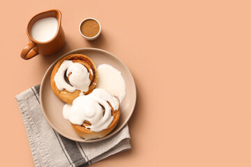 Plate of sweet cinnamon rolls with glaze and jug of milk on brown background