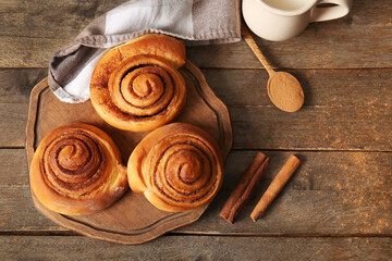 Board with sweet cinnamon rolls on wooden background