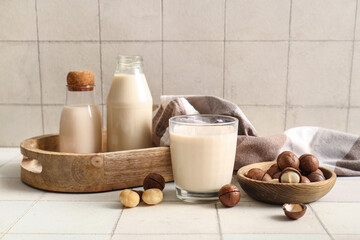 Glass and bottles of fresh macadamia milk on white tile background
