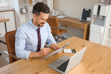 Male accountant working with clipboard at table in office