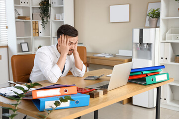 Stressed male accountant working at table in office