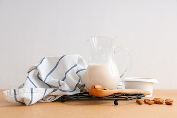 Jug of fresh almond milk and nuts on beige table