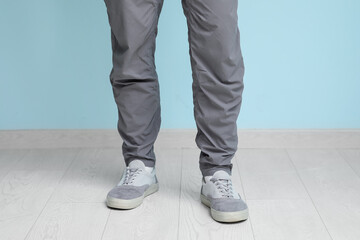 Young man in stylish sneakers near blue wall, closeup