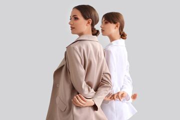 Beautiful young fashionable sisters in stylish outfits on grey background