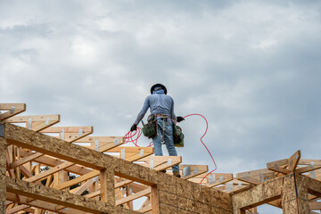 New residential home construction in framing stage, workman with hardhat and toolbelt on the roof...