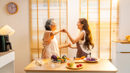 Happy Asian family cooking and having dinner together at home. Senior mother and adult daughter enjoy and fun with healthy lifestyle singing and dancing together during preparing food in the kitchen.