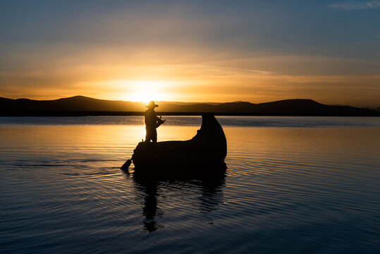 Man in traditional costume sailing in a traditional boat on lake titicaca at sunset puno peru
