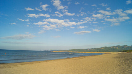 A white sandy beach at Bagac, Bataan, Philippines; overlooking the vast blue water and sky of Bagac Bay. A mountain range surrounds the area, visibly in the distance.    