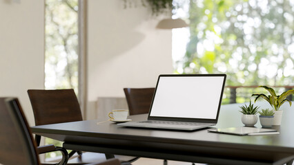 A laptop with a white-screen mockup on a hardwood meeting table in a bright modern meeting room.