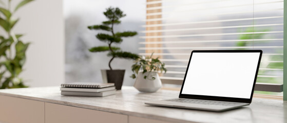 A laptop white-screen mockup on a grey marble table in a contemporary bright room.