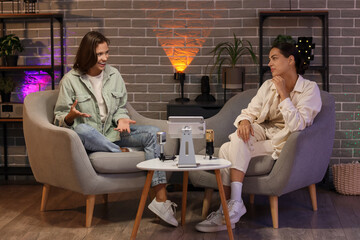 Young women on armchairs recording podcast in studio at night