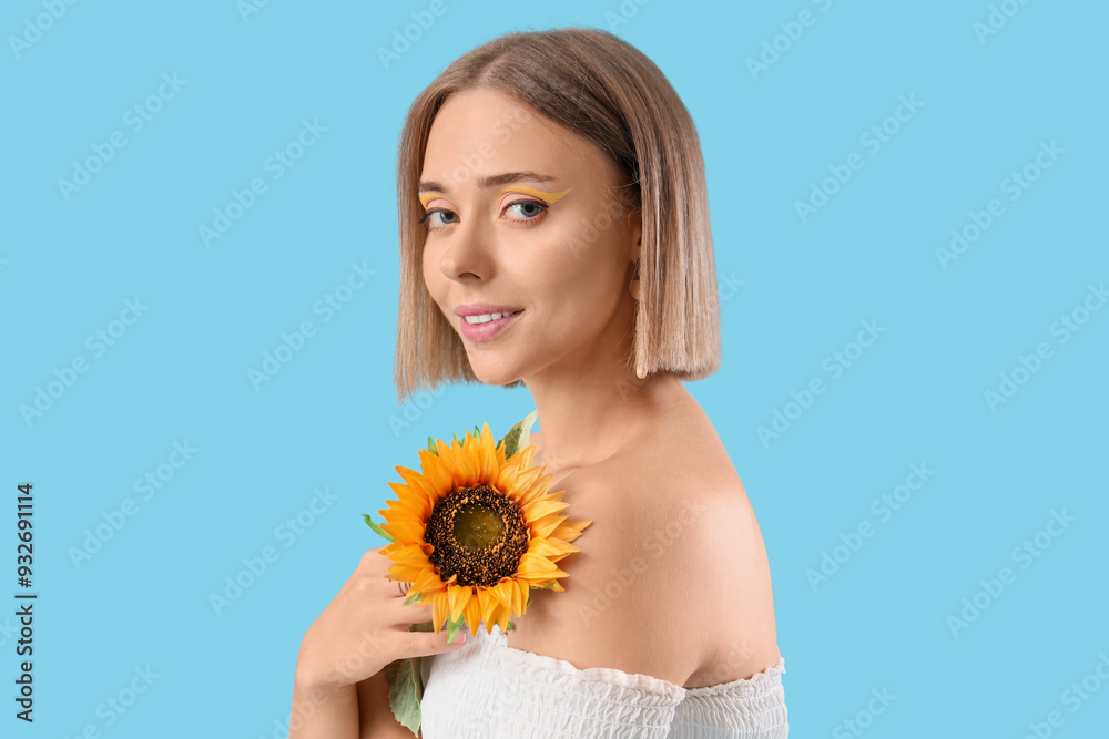 Wall mural Beautiful young happy woman with stylish makeup and sunflowers on blue background