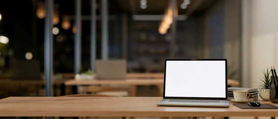 A laptop on a wooden table in a contemporary minimalist coffee shop co-working space at night.