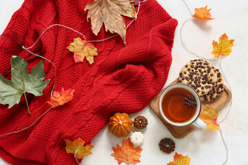 Composition with cup of tea, cookies, stylish sweater and autumn leaves on light background