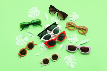 Different stylish sunglasses and palm leaves made of paper on green background