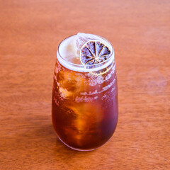 Refreshing iced coffee beverage is being mixed in a tall glass with a dried citrus fruit for garnish