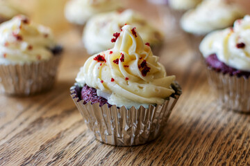 Red velvet cupcakes in silver foil on a wooden table.