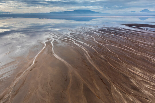 Africa, Tanzania, Aerial view of streams winding along shore of Lake Natron and distant Ol Doinyo Lengai volcano