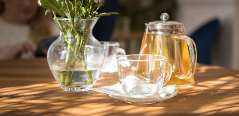 A table with a vase of flowers, a tea pot, and a cup